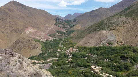 Village buildings and green trees fill the Imlil valley between steep, brown mountain slopes.