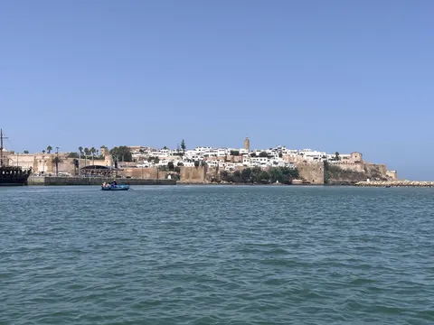 Ochre ramparts and white houses of the Kasbah of the Oudayas rise above blue water, with a small boat in front.