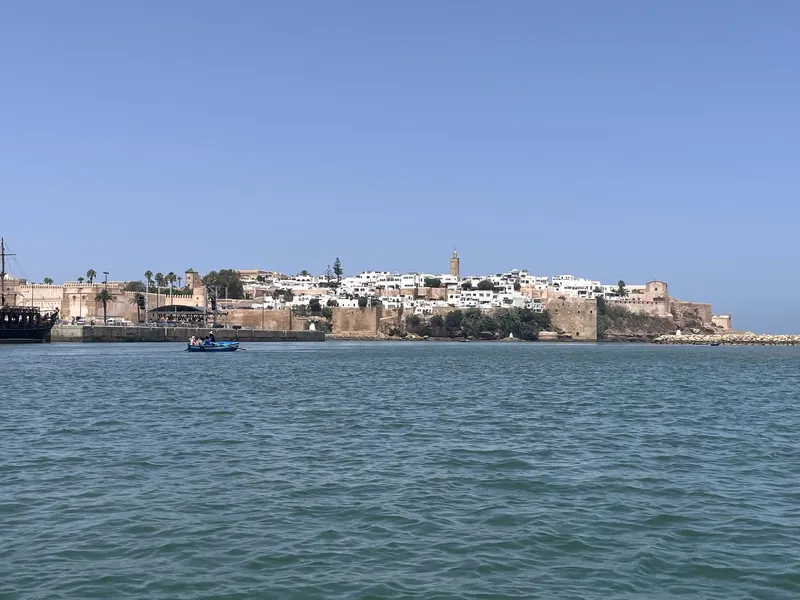 Ochre ramparts and white houses of the Kasbah of the Oudayas rise above blue water, with a small boat in front.