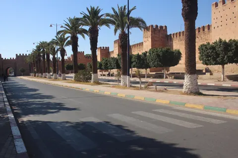 Ochre crenellated walls and towers run beside a palm-lined street in Taroudant.